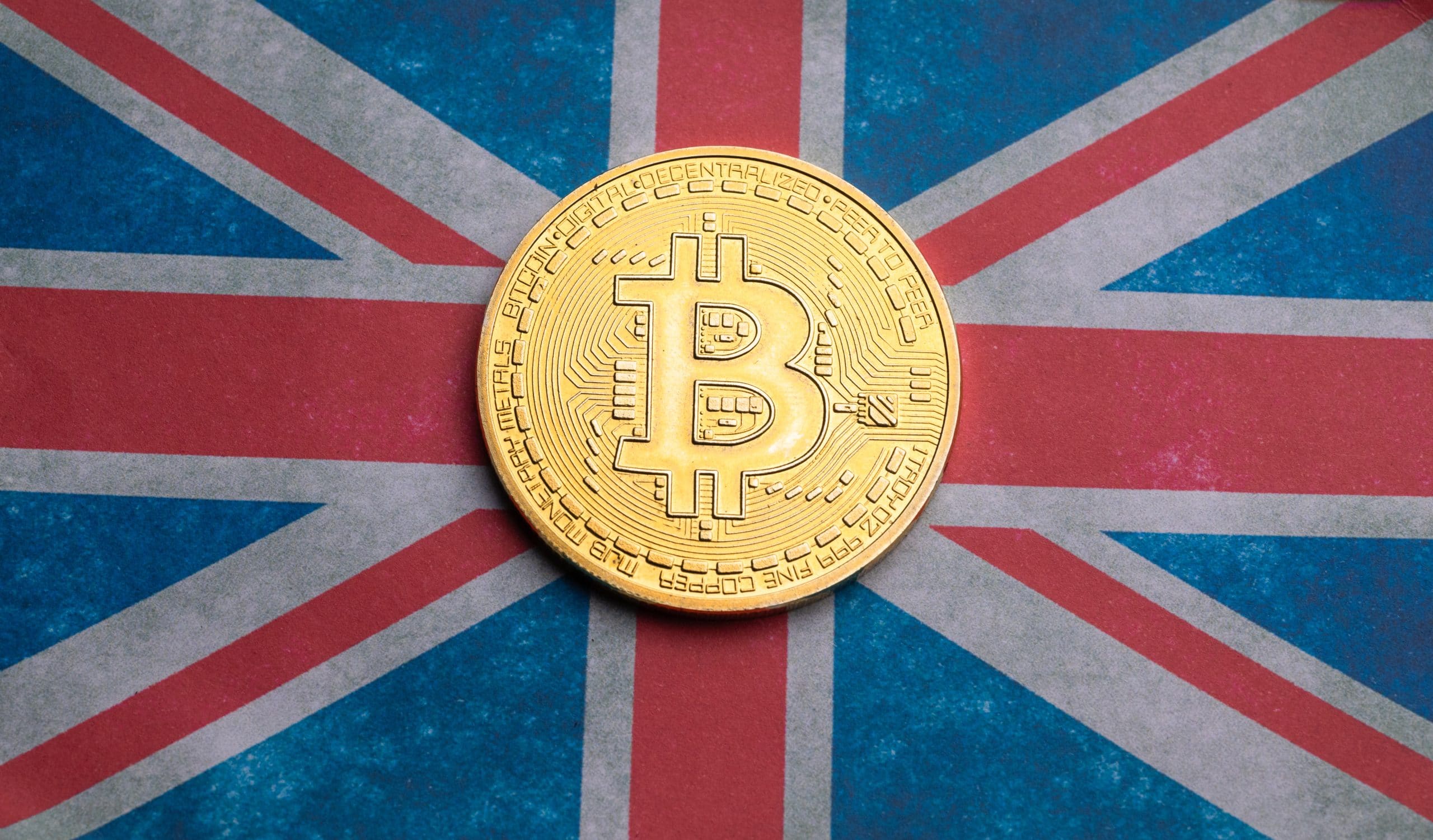 Eine goldene Bitcoin-Münze glänzt auf einer Oberfläche, die mit dem ikonischen Design der Flagge des Vereinigten Königreichs verziert ist und die Verschmelzung von traditionellem Erbe und innovativen Krypto-Trends symbolisiert.