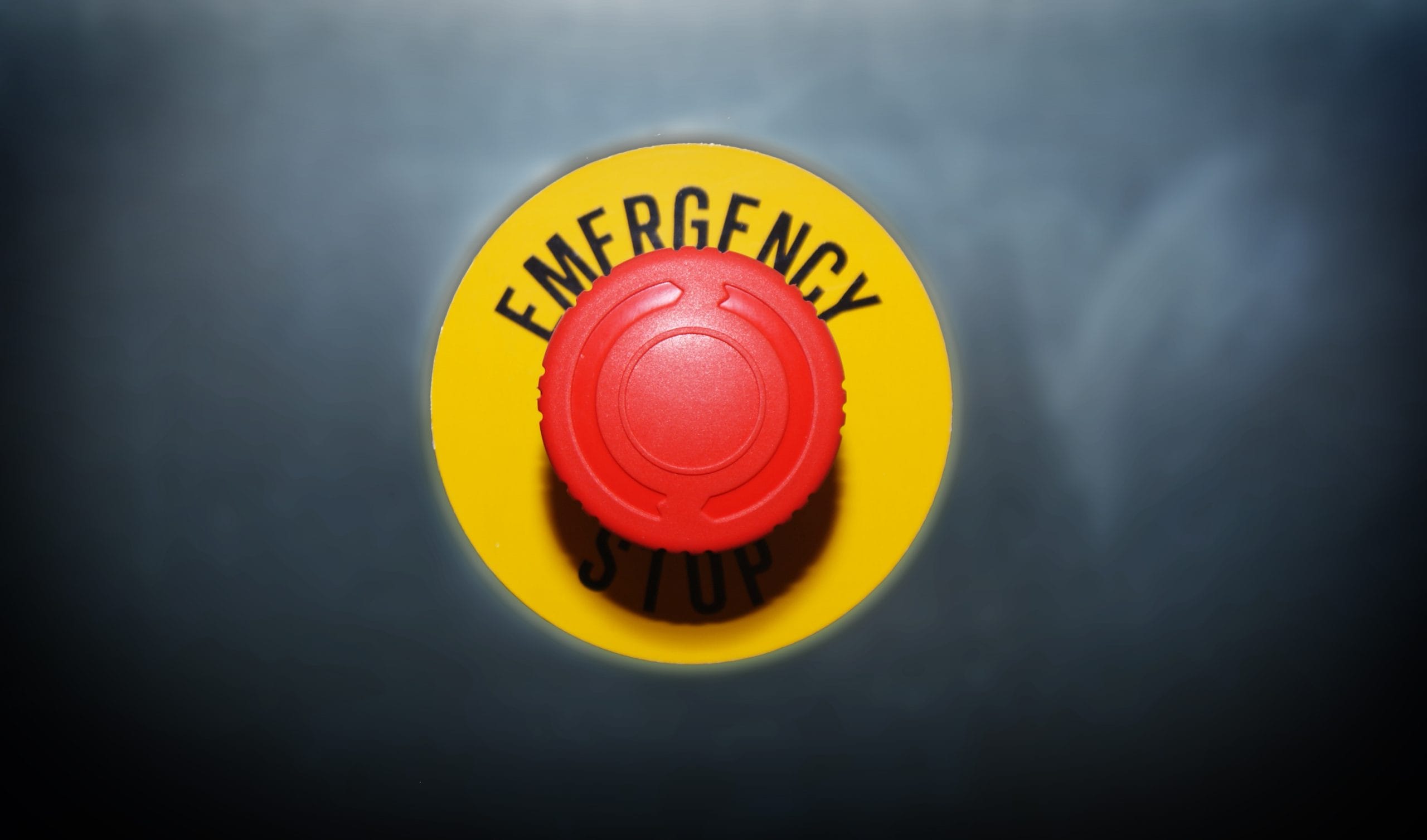 Der rote Not-Aus-Knopf sitzt gut sichtbar auf einem gelben Sockel und ist mit den Worten „EMERGENCY STOP“ (Not-Aus) versehen