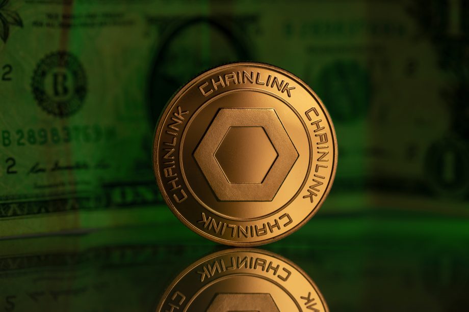 Eine goldfarbene Chainlink-Kryptowährungsmünze steht aufrecht auf einer spiegelnden Oberfläche mit einer verschwommenen US-Dollar-Note im Hintergrund und symbolisiert den raschen Fortschritt im digitalen Finanzwesen.