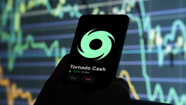 Tornado Cash Logo auf einem Smartphone, das vor einen Kurs-Graphen gehalten wird.