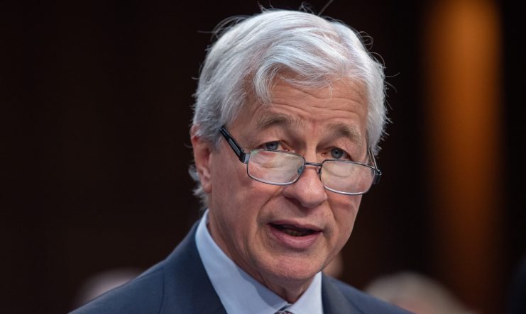 Ein älterer Mann mit grauem Haar und Brille, Anzug und Krawatte, spricht nachdenklich. Der Hintergrund ist unscharf und suggeriert ein professionelles Ambiente – möglicherweise eine Veranstaltung oder Konferenz von JPMorgan.