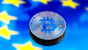 Eine physische Bitcoin-Münze liegt auf einem blauen Hintergrund mit gelben Sternen, die der Flagge der Europäischen Union ähneln und die wachsende Verbindung zwischen Krypto und der europäischen Finanzlandschaft symbolisieren.