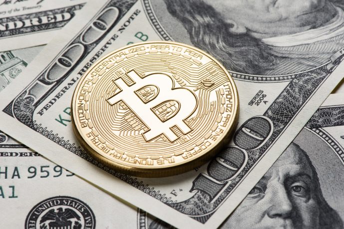 Eine glänzende goldene Bitcoin-Münze liegt auf einem Stapel US-Dollarscheine, darunter ein gut sichtbarer 100-Dollar-Schein, und veranschaulicht die Mischung aus traditioneller und digitaler Währung.