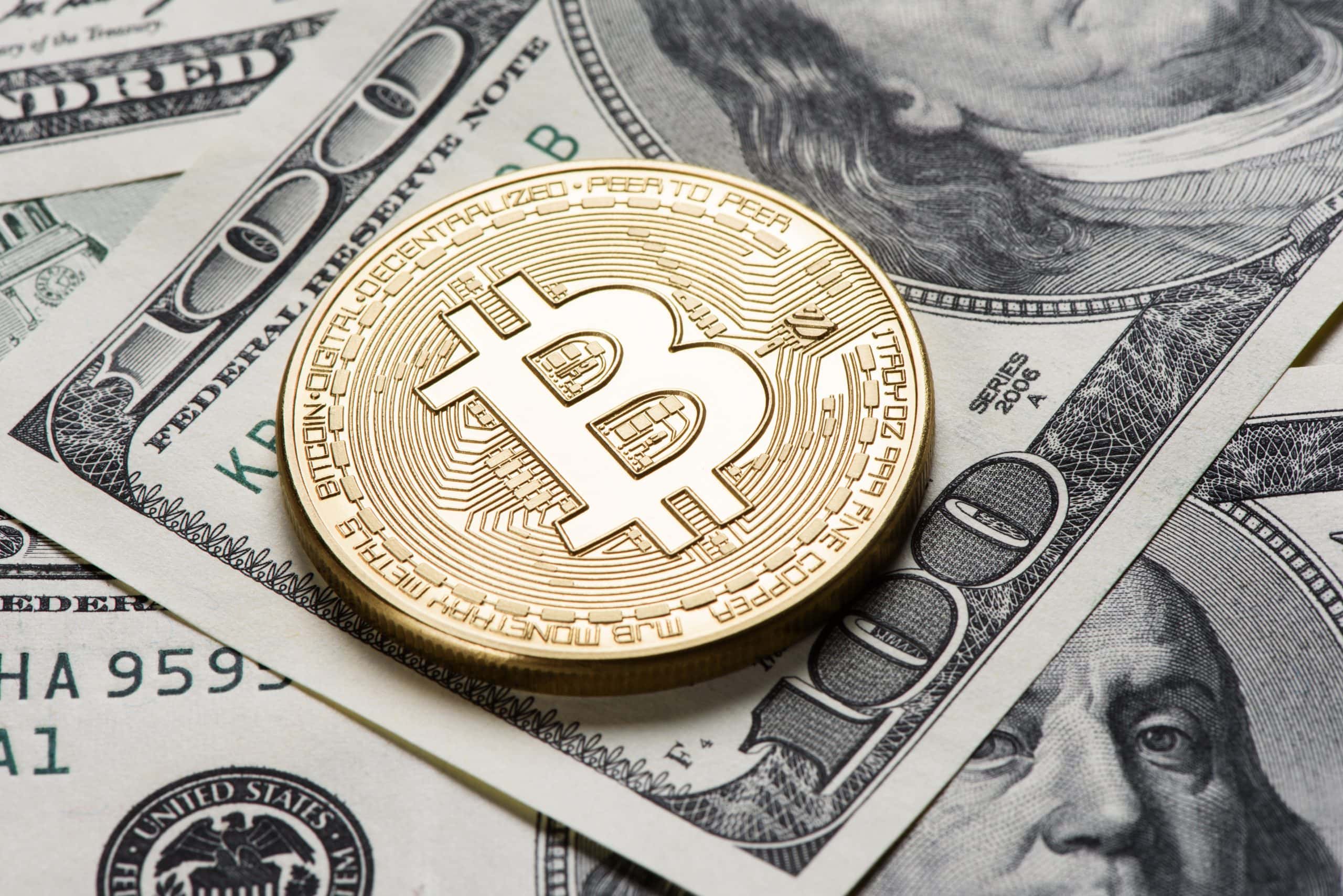 Eine glänzende goldene Bitcoin-Münze liegt auf einem Stapel US-Dollarscheine, darunter ein gut sichtbarer 100-Dollar-Schein, und veranschaulicht die Mischung aus traditioneller und digitaler Währung.