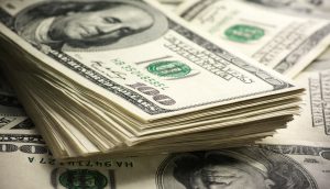 Ein Stapel US-amerikanischer Hundertdollarscheine mit dem Porträt Benjamin Franklins ist auf weiteren verstreuten Scheinen abgebildet.