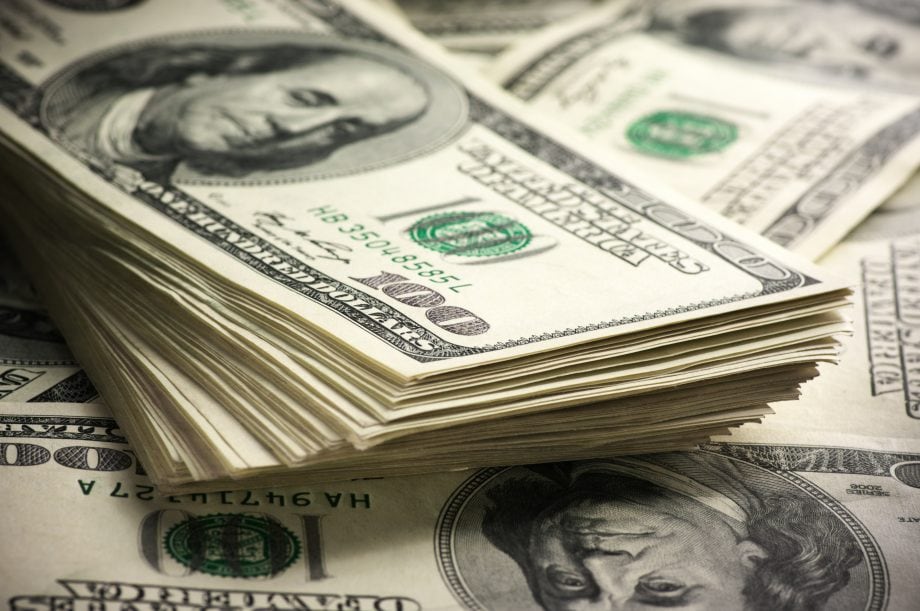 Ein Stapel US-amerikanischer Hundertdollarscheine mit dem Porträt Benjamin Franklins ist auf weiteren verstreuten Scheinen abgebildet.