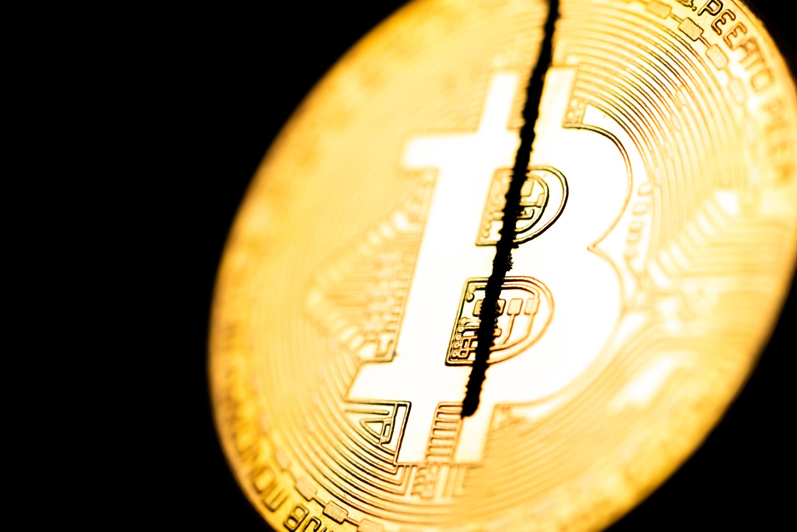 Nahaufnahme einer goldenen Bitcoin-Münze mit einem auffälligen Riss in der Mitte, der vor einem schwarzen Hintergrund Instabilität oder Spaltung nach der Halbierung symbolisiert.