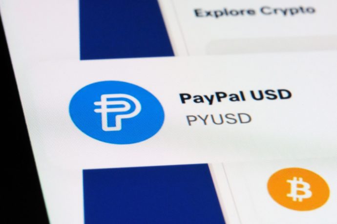 Auf einem digitalen Bildschirm werden das Logo und der Name von Paypal USD (PYUSD) angezeigt. Darunter ist ein Teil eines Bitcoin-Symbols sichtbar, was die Präsenz von Paypal in der Welt der digitalen Währungen unterstreicht.