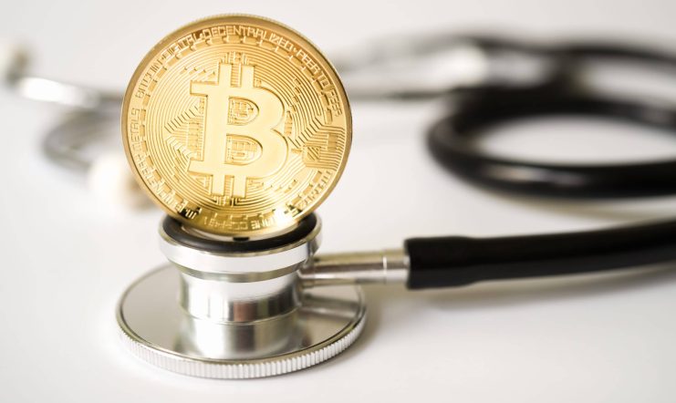 Eine goldene Bitcoin-Münze liegt auf der Membran eines Stethoskops und symbolisiert die wachsende Beziehung zwischen Bitcoin und der modernen Gesundheitsversorgung.