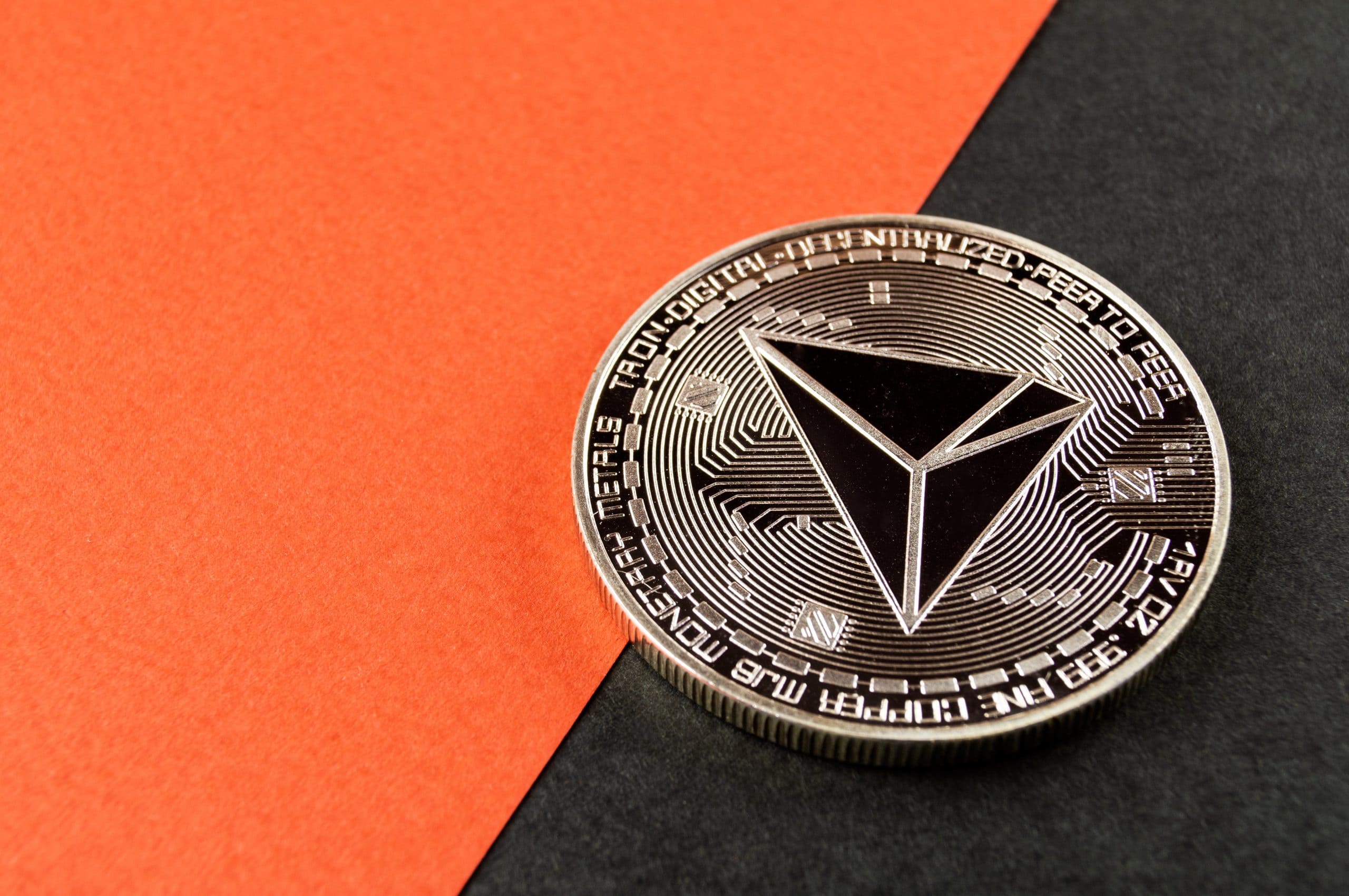 Eine Tron-Kryptowährungsmünze sitzt prominent auf einem diagonalen roten und schwarzen Hintergrund und ruft den nervösen Reiz einer Memecoin-Sensation hervor.