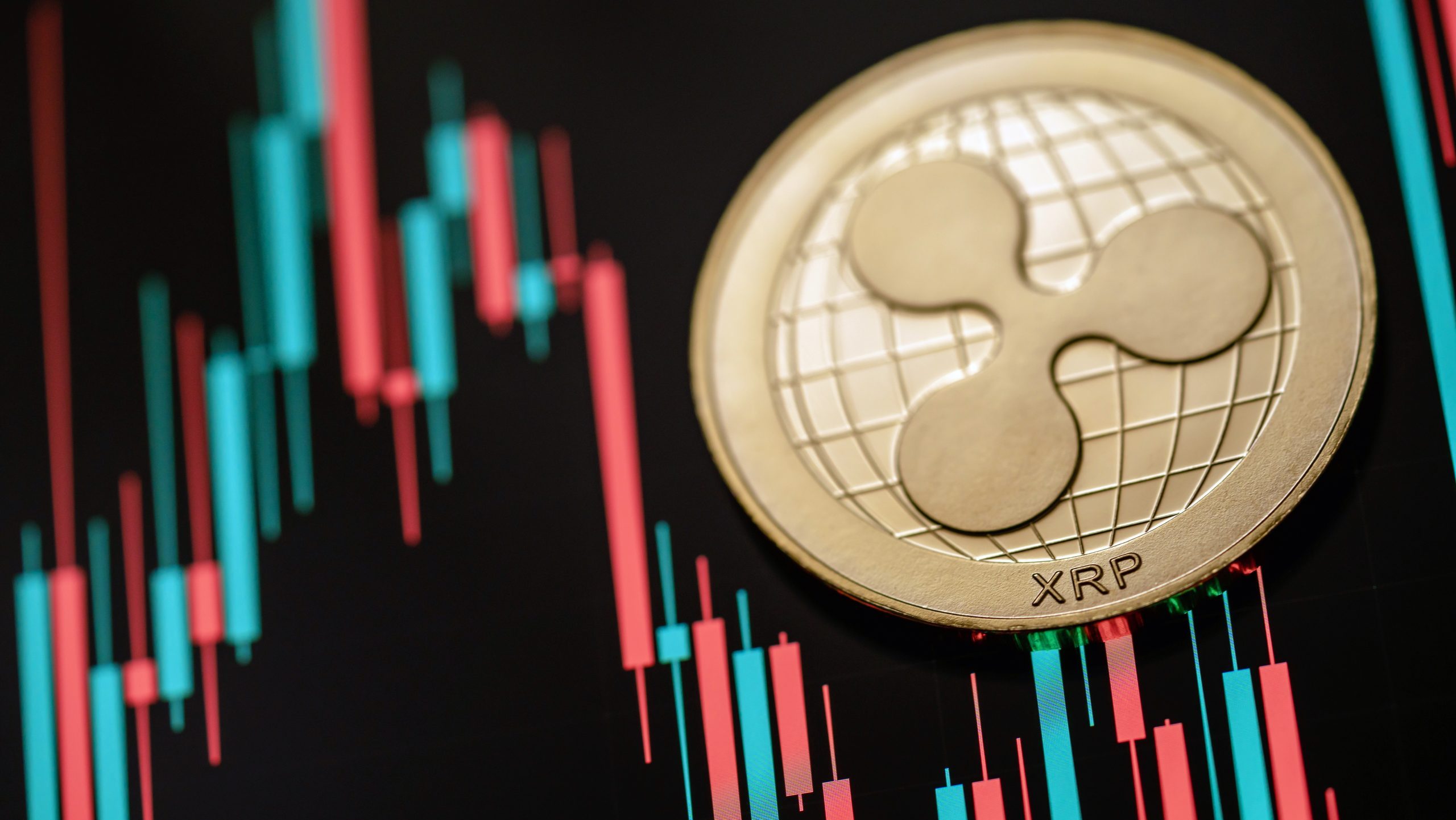 Eine goldene XRP-Münze, die das digitale Vermögen von Ripple darstellt, wird neben roten und grünen Candlestick-Charts auf schwarzem Hintergrund angezeigt.