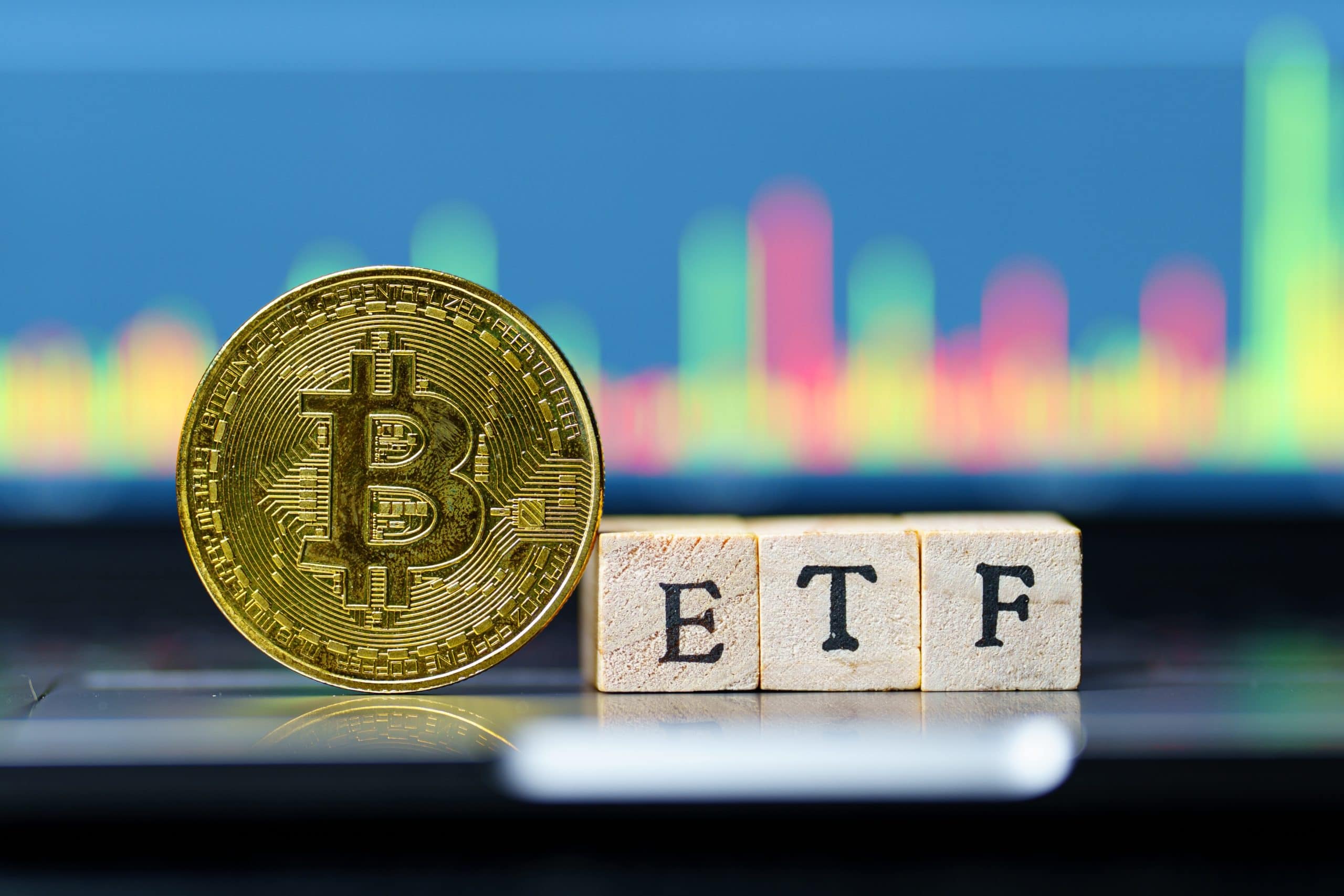 Eine goldene Bitcoin-Münze steht neben Holzklötzen mit der Aufschrift „ETF“. Im Hintergrund ist ein buntes, unscharfes Finanzdiagramm zu sehen, das die wachsende Rolle von Bitcoin bei ETF-Investitionen hervorhebt.