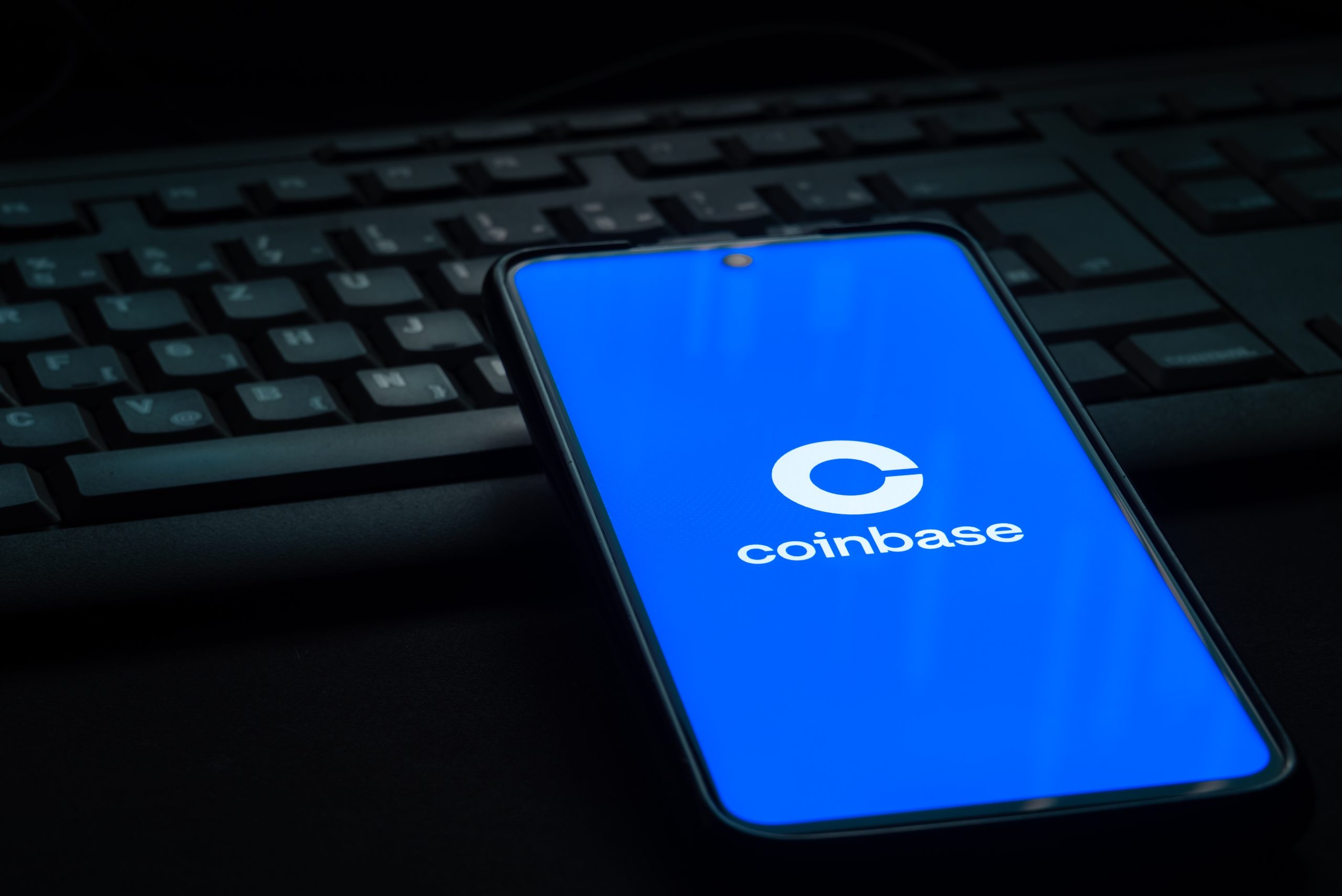 Smartphone mit Coinbase-Logo auf Display liegt auf Tastatur