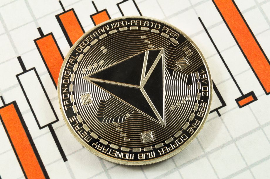 Eine Münze mit dem Emblem der Kryptowährung Tron liegt auf einem Diagramm mit orangefarbenen und schwarzen Balken.