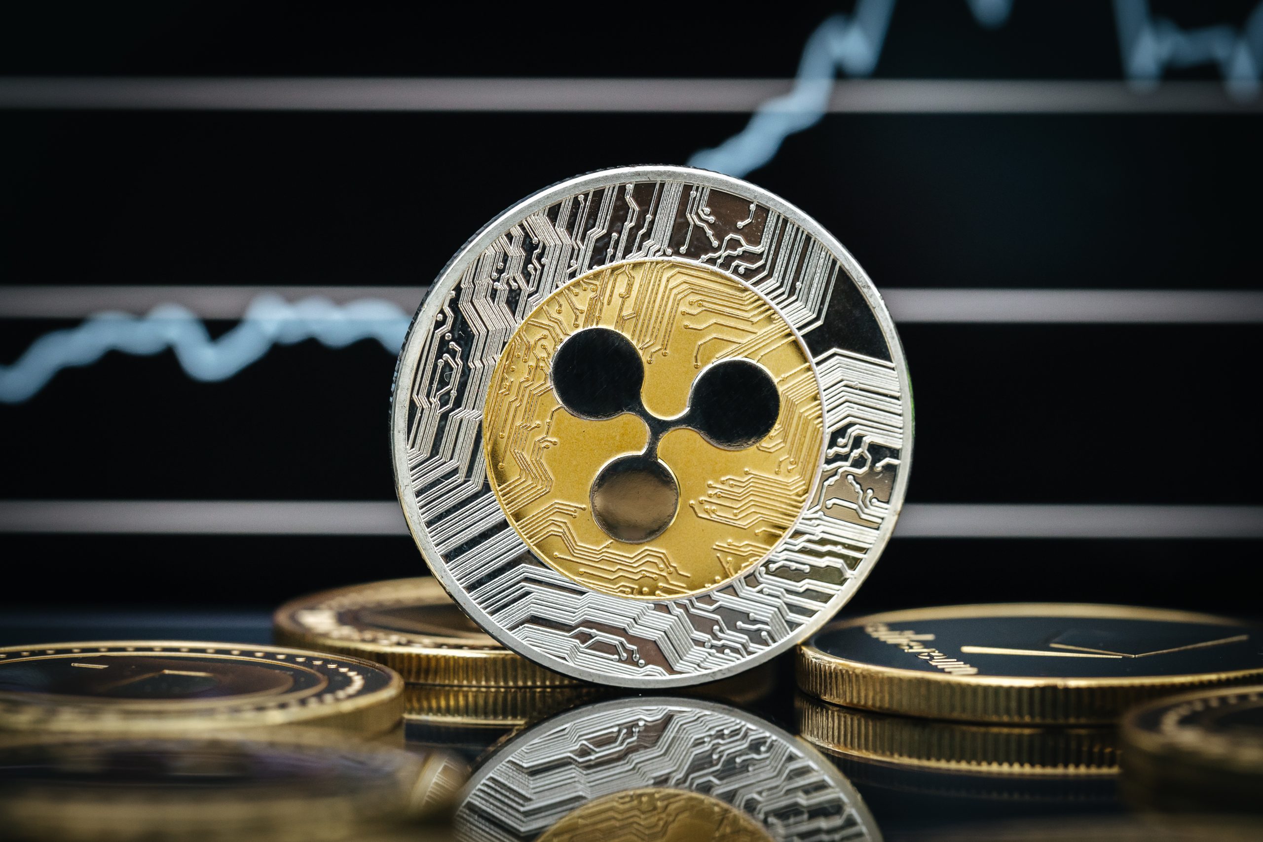 Eine Ripple-Münze (XRP) sticht stolz zwischen anderen Münzen hervor, ihre glänzende Oberfläche spiegelt das dynamische Finanzdiagramm im unscharfen Hintergrund wider.