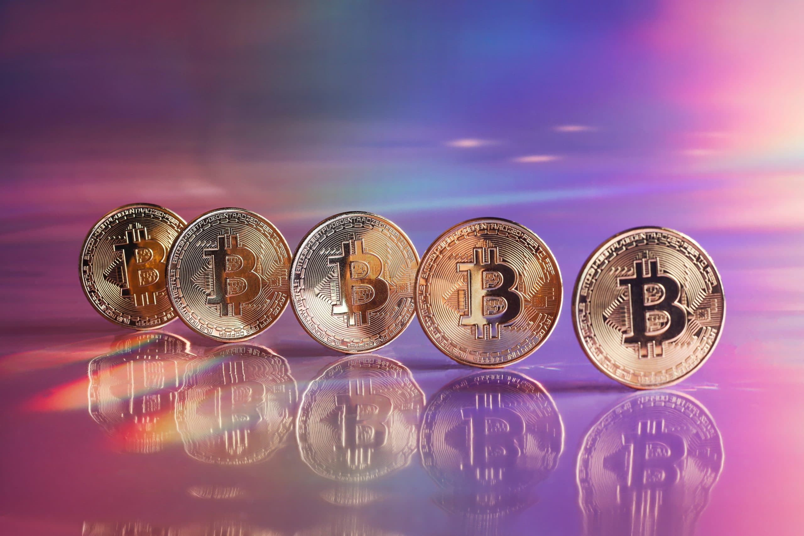 Ein lebendiger, reflektierender Hintergrund bildet die Bühne für fünf glänzende Bitcoin-Münzen, die perfekt in einer fesselnden Reihe angeordnet sind.