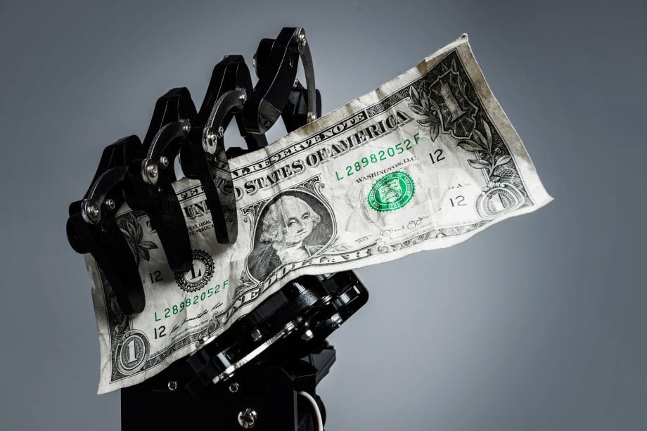 Roboterhand hält US-Dollar-Schein als Symbol für Stablecoins, KI-Agenten und digitale Zahlungen