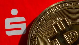 Eine Nahaufnahme einer Bitcoin-Münze, die das ikonische weiße Sparkassensymbol auf einem kräftigen roten Hintergrund teilweise verdeckt.