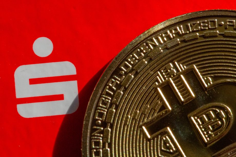 Eine Nahaufnahme einer Bitcoin-Münze, die das ikonische weiße Sparkassensymbol auf einem kräftigen roten Hintergrund teilweise verdeckt.