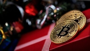 Zwei Bitcoin-Münzen liegen auf einem verpackten Geschenk neben Christbaumkugeln.