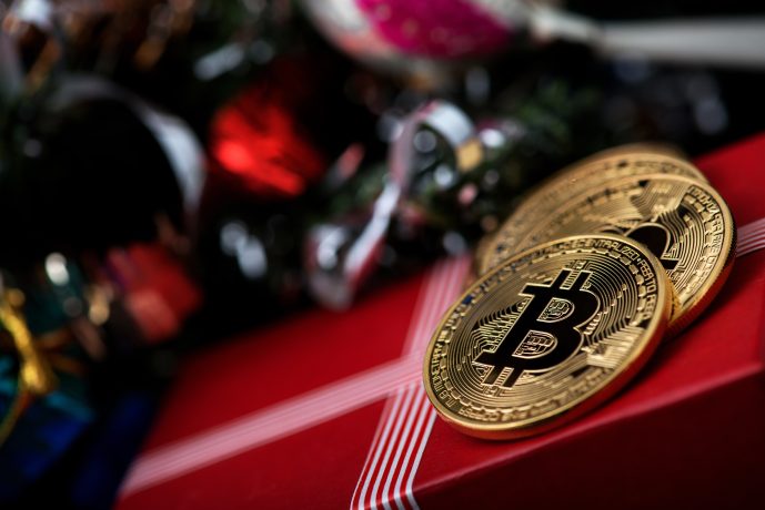 Zwei Bitcoin-Münzen liegen auf einem verpackten Geschenk neben Christbaumkugeln.
