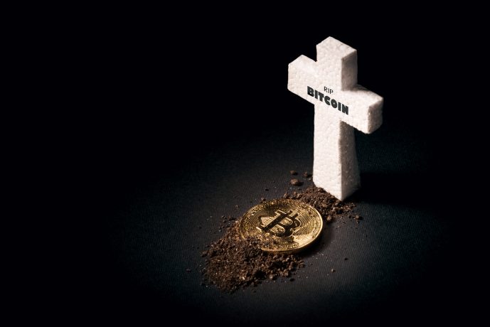Ein goldener Bitcoin liegt teilweise mit Erde bedeckt neben einem weißen, kreuzförmigen Grabstein mit der Aufschrift „RIP BITCOIN“, der auf dunklem Hintergrund das ungewisse Schicksal von Bitcoin symbolisiert.