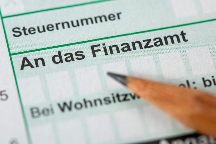 Nahaufnahme eines deutschen Steuerformulars mit einem Bleistift, der auf den Satz „An das Finanzamt“ zeigt, neben Feldern für Steuerzahlerinformationen. Es gibt ein Kontrollkästchen zur Angabe von Bitcoin-Vermögen, was moderne finanzielle Überlegungen im heutigen digitalen Zeitalter widerspiegelt.
