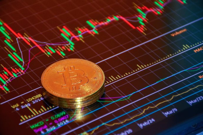 Eine physische Bitcoin-Münze liegt auf einem digitalen Bildschirm, auf dem farbenfrohe Bitcoin-Preisdiagramme und dynamische Handelsdaten für Kryptowährungen angezeigt werden.