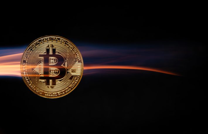 Im Vordergrund glänzt eine Bitcoin-Münze, die vor einem schattigen Hintergrund eine lebendige Bewegungsspur erzeugt.