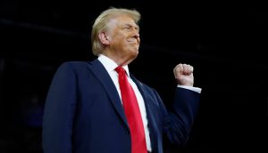 Der US-Präsident Donald Trump steht mit erhobener rechter Faust und einem leichten Lächeln vor einem dunklen Hintergrund.