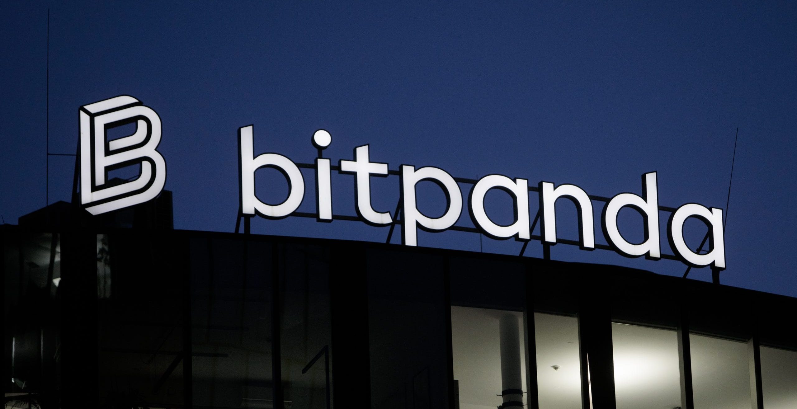 Das Bitpanda-Logo leuchtet hell auf der Gebäudefassade und wirft einen leuchtenden Kontrast zum Nachthimmel.