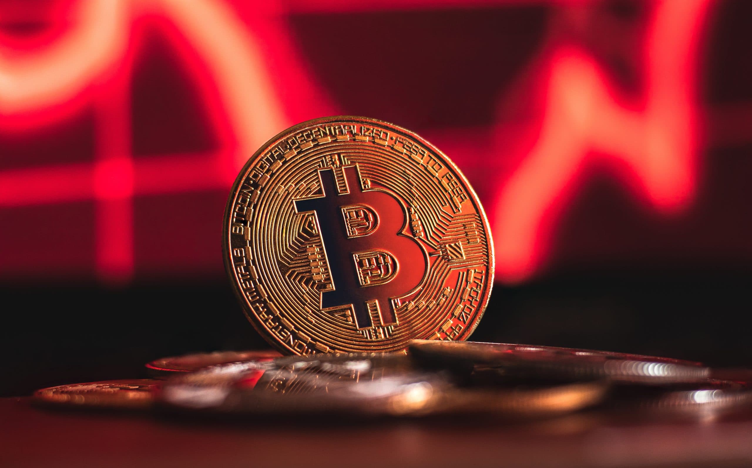 Ein Bitcoin glänzt auf einem Stapel Münzen vor dem Hintergrund eines dynamischen roten Finanzdiagramms, das seine volatile Natur widerspiegelt.