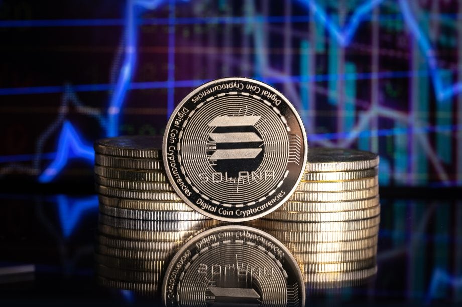 Im Vordergrund ist deutlich ein Stapel Solana-Münzen zu sehen, im Hintergrund ein verschwommenes digitales Finanzdiagramm.