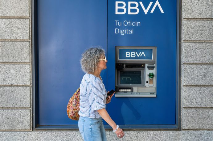 Eine Person geht an einem in die Wand eingelassenen BBVA-Geldautomaten vorbei und denkt über den Aufstieg von Bitcoin und seine Auswirkungen auf den modernen Handel nach.