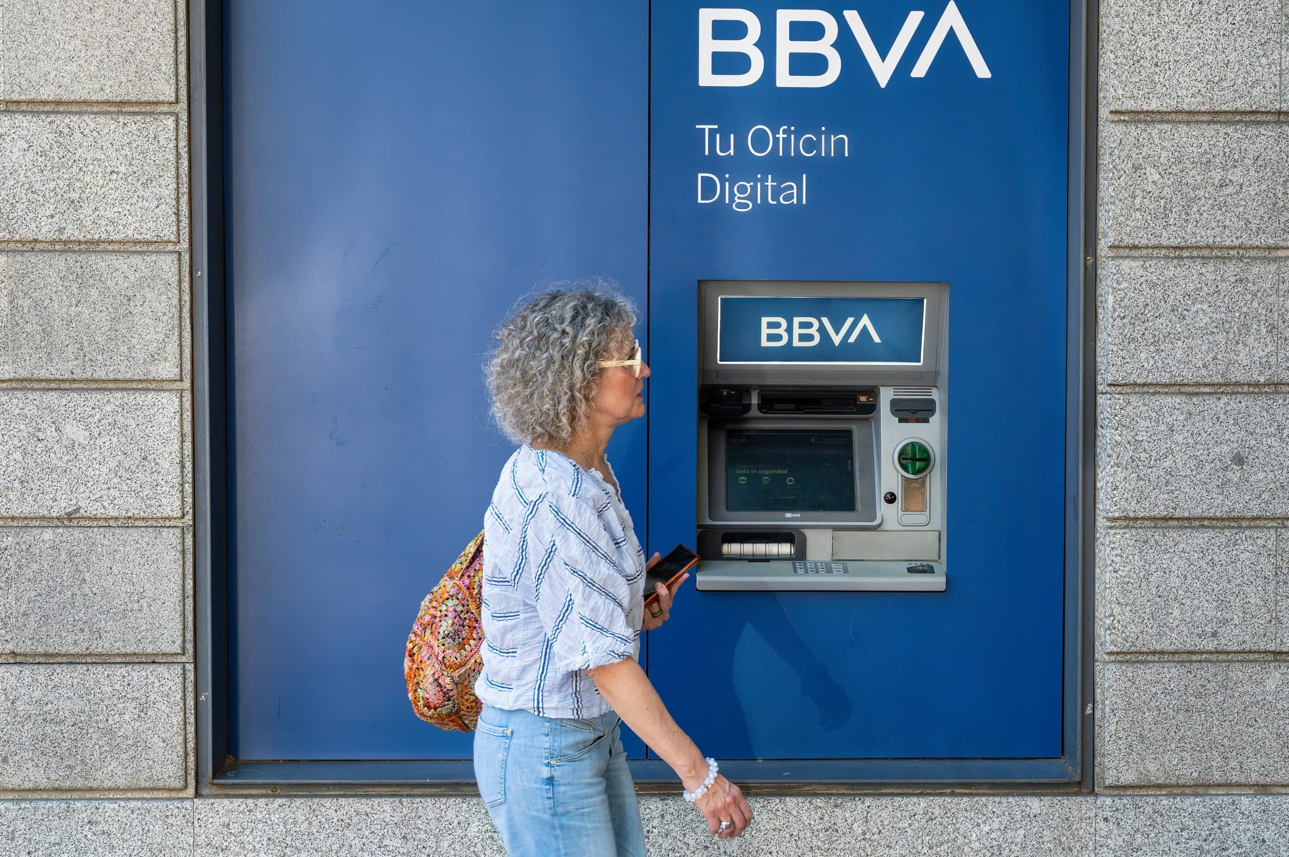 Eine Person geht an einem in die Wand eingelassenen BBVA-Geldautomaten vorbei und denkt über den Aufstieg von Bitcoin und seine Auswirkungen auf den modernen Handel nach.