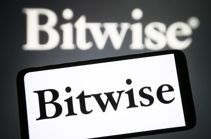 Auf einem Smartphone wird das Logo von „Bitwise“ plastisch dargestellt, im Hintergrund ist eine unscharfe Projektion des Krypto-Indexfonds des Vermögensverwalters zu sehen.