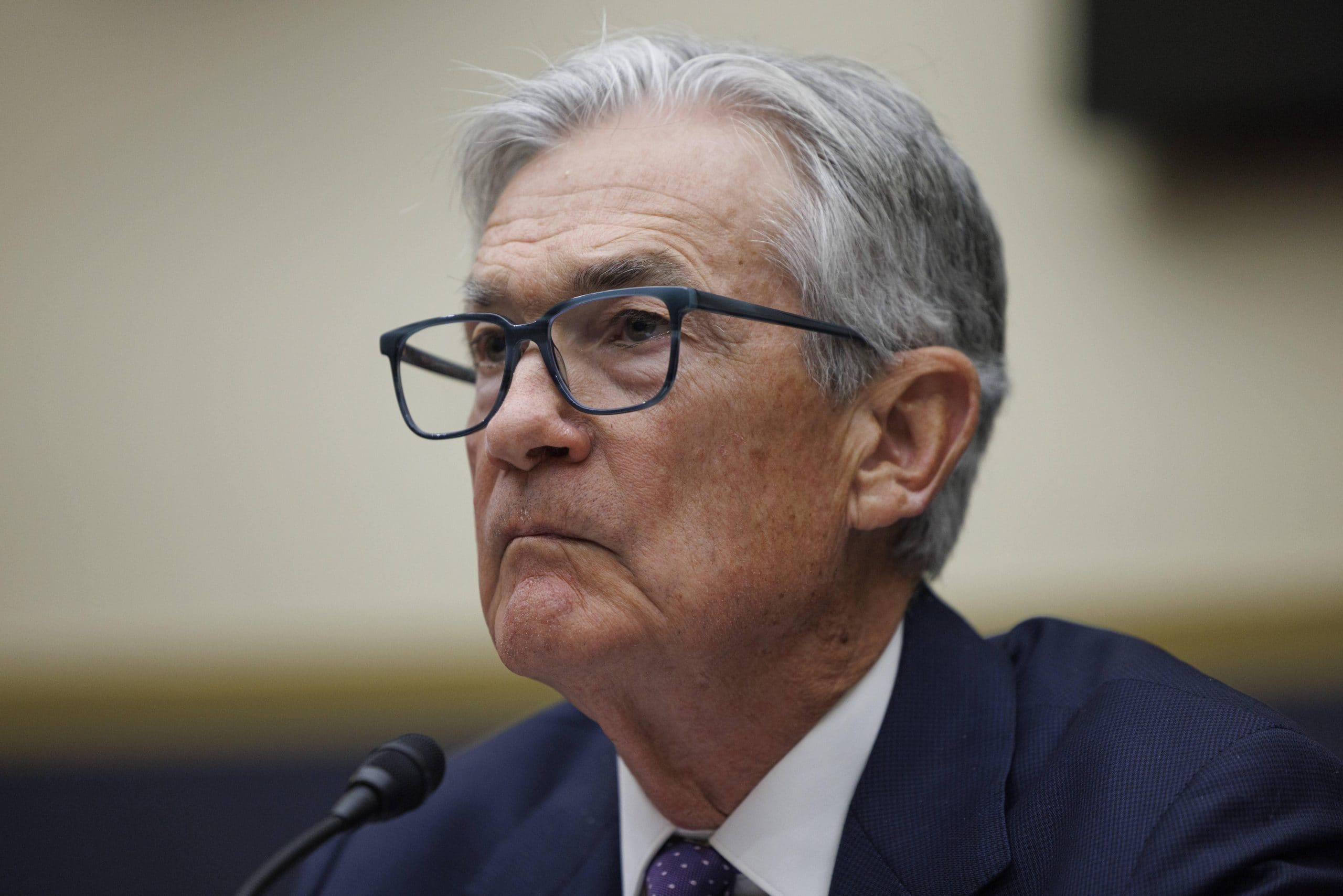 Ein älterer Mann mit grauem Haar und Brille spricht in ein Mikrofon über die Inflation. Er trägt einen dunklen Anzug und eine blaue Krawatte.