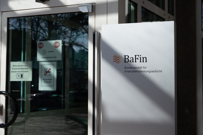 Eingang zum BaFin-Büro mit Glastür, Schild mit der Aufschrift „Bundesanstalt für Finanzdienstleistungsaufsicht“ und Warnhinweisen.