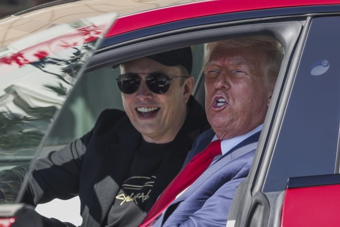 Zwei Männer sitzen in einem geparkten Auto. Einer lässt mit schwarzer Kappe und Sonnenbrille seinen inneren Elon Musk rüber, während der andere in Anzug und roter Krawatte elegante Professionalität verkörpert.