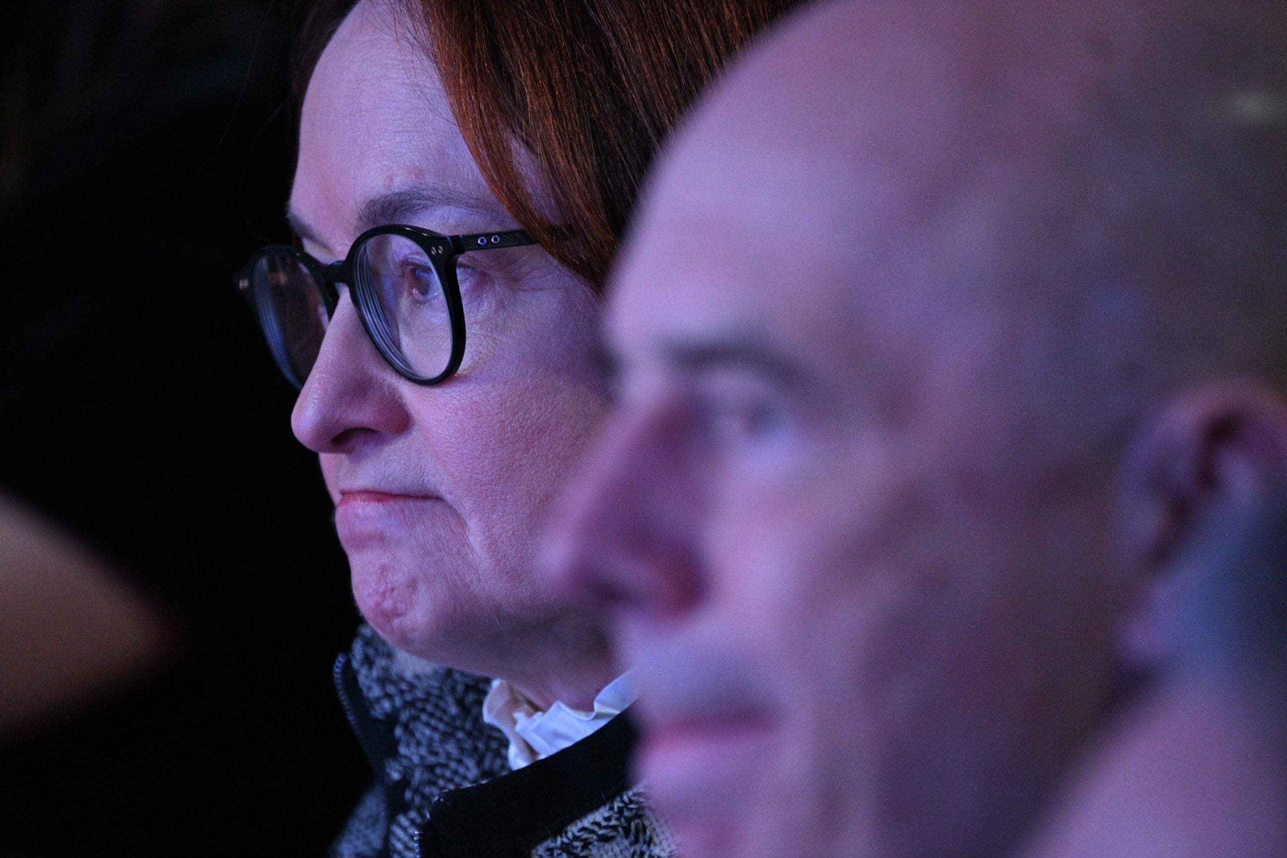 Eine Frau mit Brille und ein Mann sitzen dicht beieinander, beide wirken konzentriert und ernst und diskutieren möglicherweise über den Einfluss der russischen Politik auf Kryptokäufe.