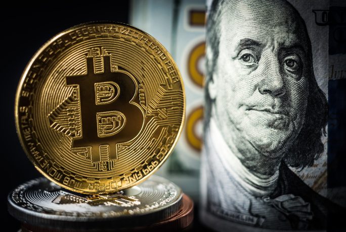 Eine glänzende Bitcoin-Münze steht stolz vor einem gerollten US-Hundert-Dollar-Schein mit dem ikonischen Porträt von Benjamin Franklin und symbolisiert die Schnittstelle zwischen traditionellen und digitalen Währungen.