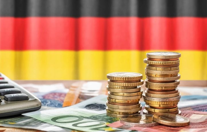 Stapel von Euromünzen und -scheinen liegen neben einem Taschenrechner, mit einem Hauch digitaler Zahlen, die auf Kryptoberechnungen hindeuten, und das alles vor dem Hintergrund der deutschen Flagge.