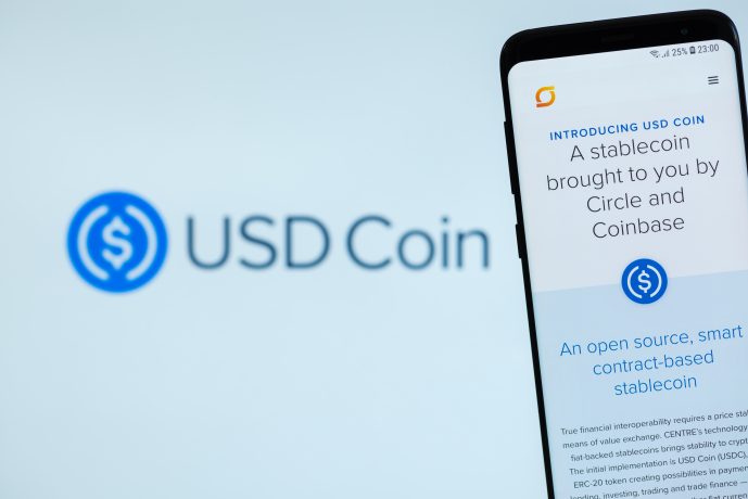 Smartphone, auf dem die USD Coin-Webseite vor einem unscharfen Hintergrund mit dem USD Coin-Logo angezeigt wird.