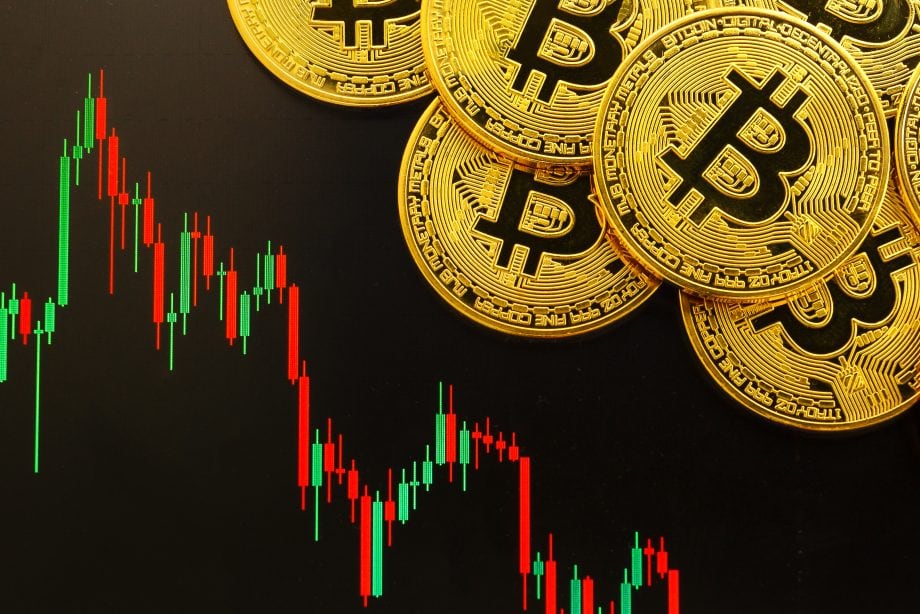 Goldfarbene Bitcoin-Münzen werden über einem digitalen Candlestick-Chart platziert, das die Bitcoin-Preisschwankungen auf schwarzem Hintergrund zeigt.