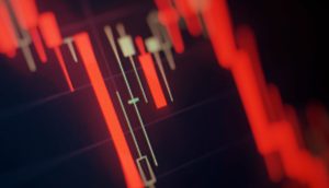 Eine Nahaufnahme eines Krypto-Candlestick-Charts in Rot zeigt einen Abwärtstrend bei den Preisen digitaler Währungen vor einem schattigen Hintergrund.