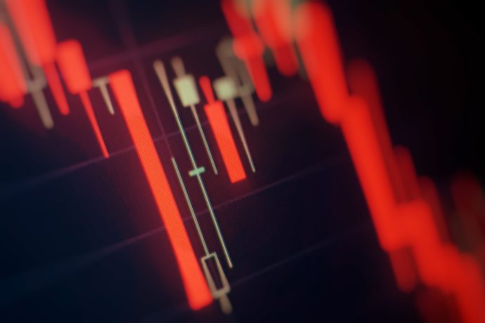 Eine Nahaufnahme eines Krypto-Candlestick-Charts in Rot zeigt einen Abwärtstrend bei den Preisen digitaler Währungen vor einem schattigen Hintergrund.