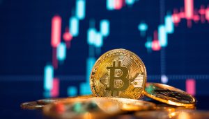 Goldene Bitcoin-Münzen sind prominent vor einem digitalen Bildschirm gestapelt, auf dem Finanzmarktdiagramme mit schwankenden Linien die dynamische Natur des Kryptowährungshandels veranschaulichen.