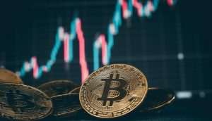 Im Vordergrund werden goldene Bitcoin-Münzen angezeigt, im Hintergrund ein unscharfes Finanzaktiendiagramm.
