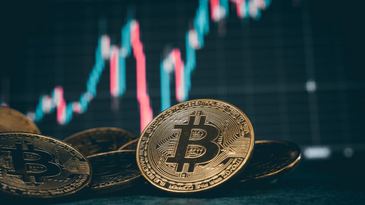 Im Vordergrund fallen glänzende Bitcoin-Münzen ins Auge, während im Hintergrund ein verschwommenes Preisdiagramm der Kryptowährung auftaucht.