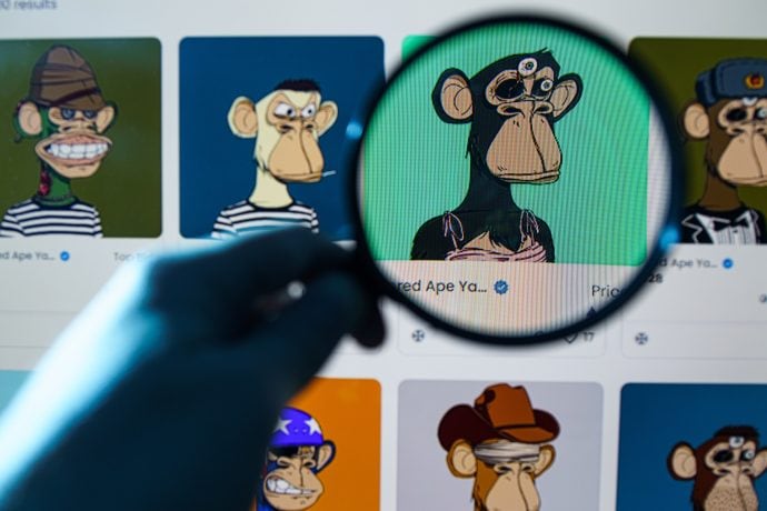Eine Person hält eine Lupe über einen Computerbildschirm, auf dem eine Sammlung illustrierter Affenfiguren angezeigt wird, als würde sie einen automatisch gespeicherten Entwurf auf versteckte Details untersuchen.
